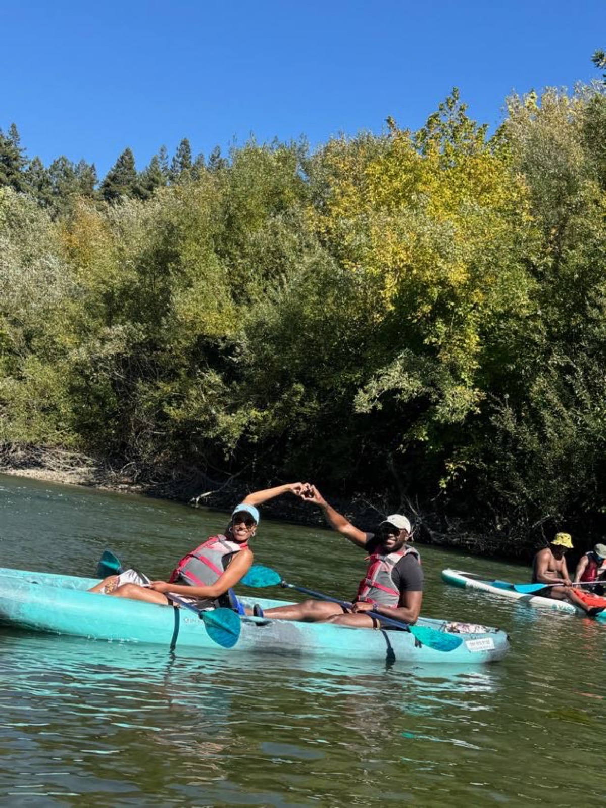 Sally and Adetunji making a heart with their hands while kayaking, September 2024